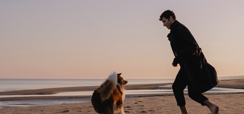 Een man aan het spelen op het strand met zijn hond
